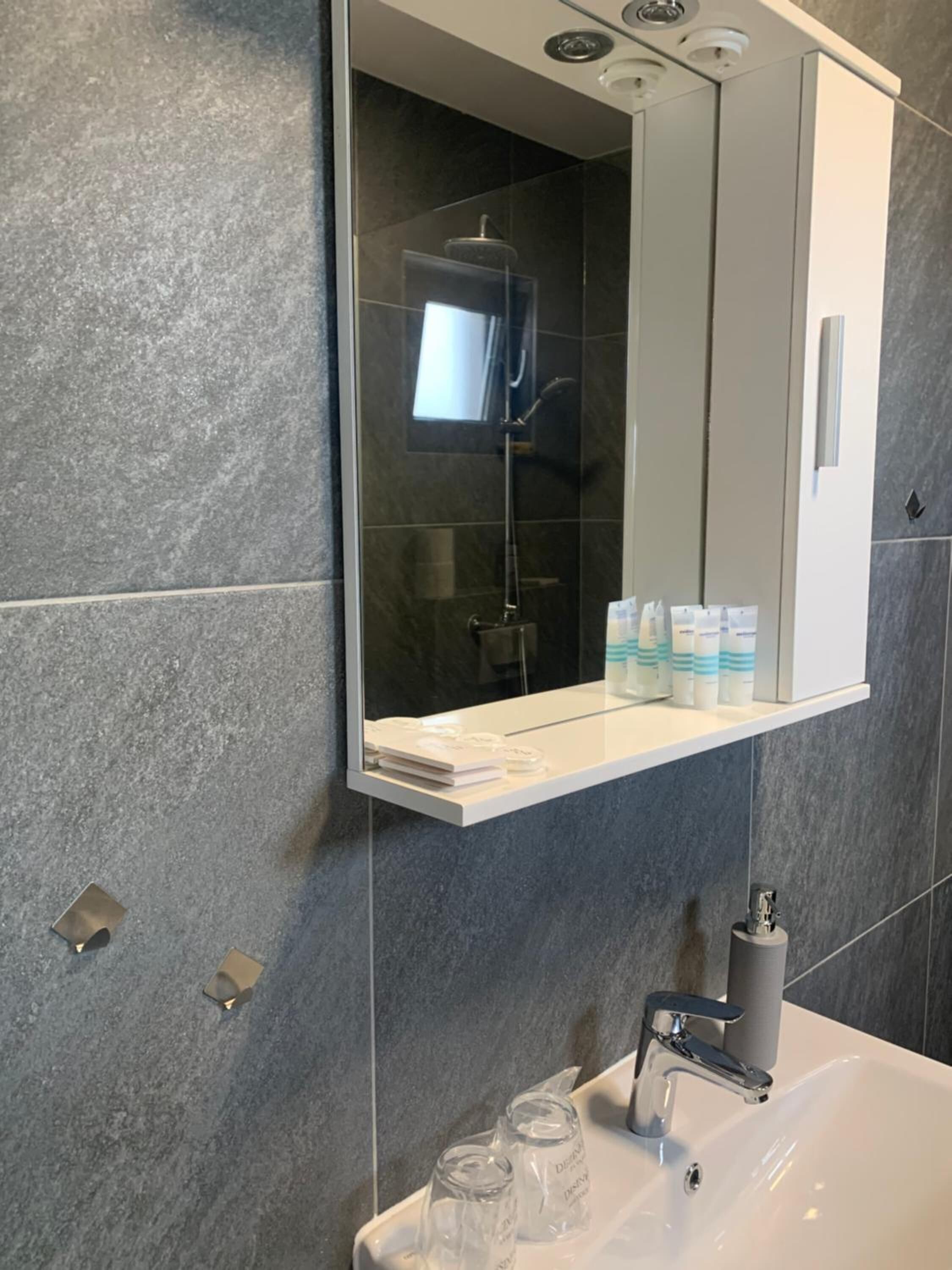 A modern bathroom with a large mirror, a shower, and a sink with a faucet.