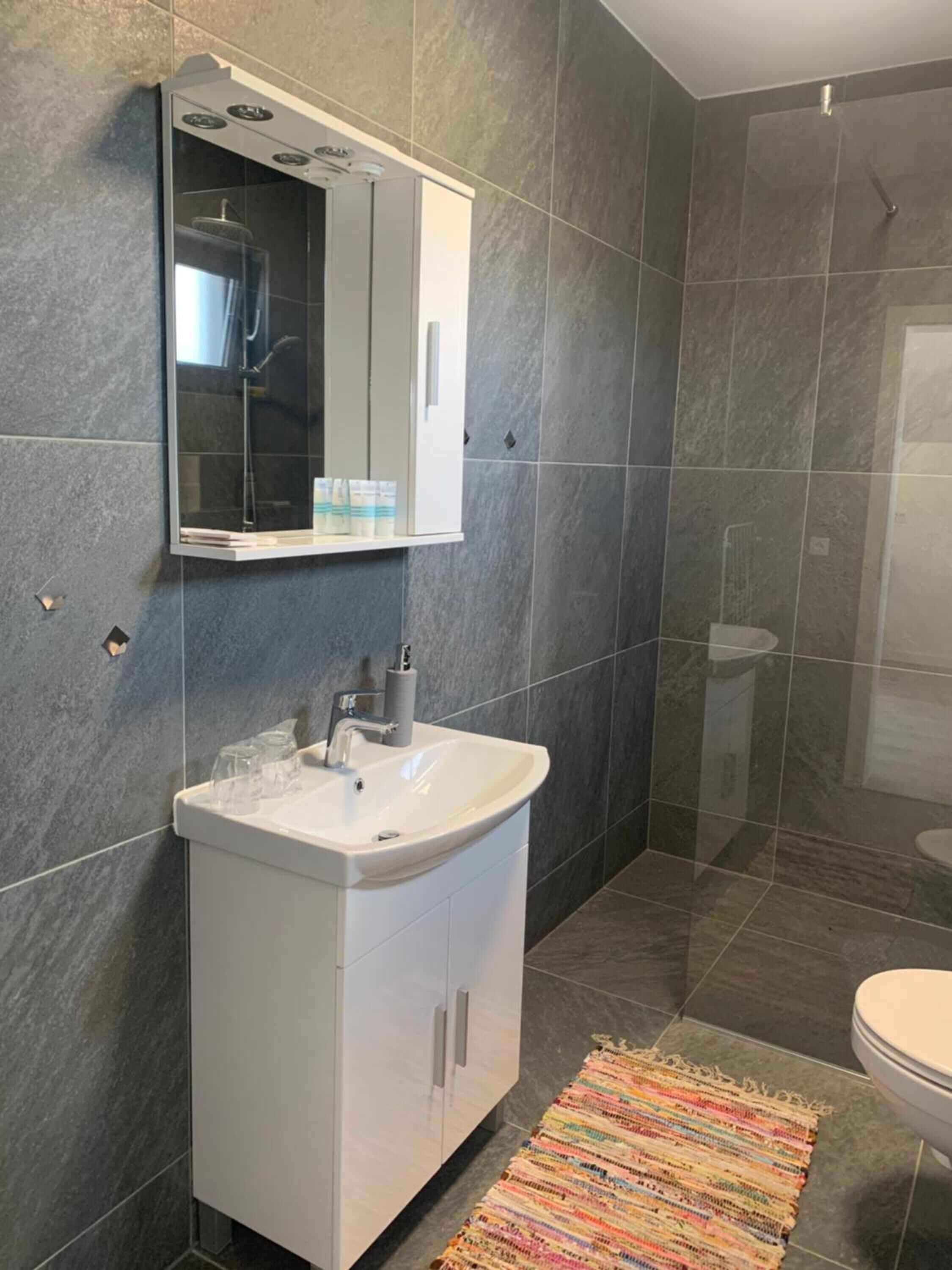 A modern bathroom with a white vanity, a large mirror, a shower enclosure, and a colorful rug.