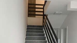 A staircase with grey tiles and a black railing, leading to a landing with a wooden slatted ceiling.