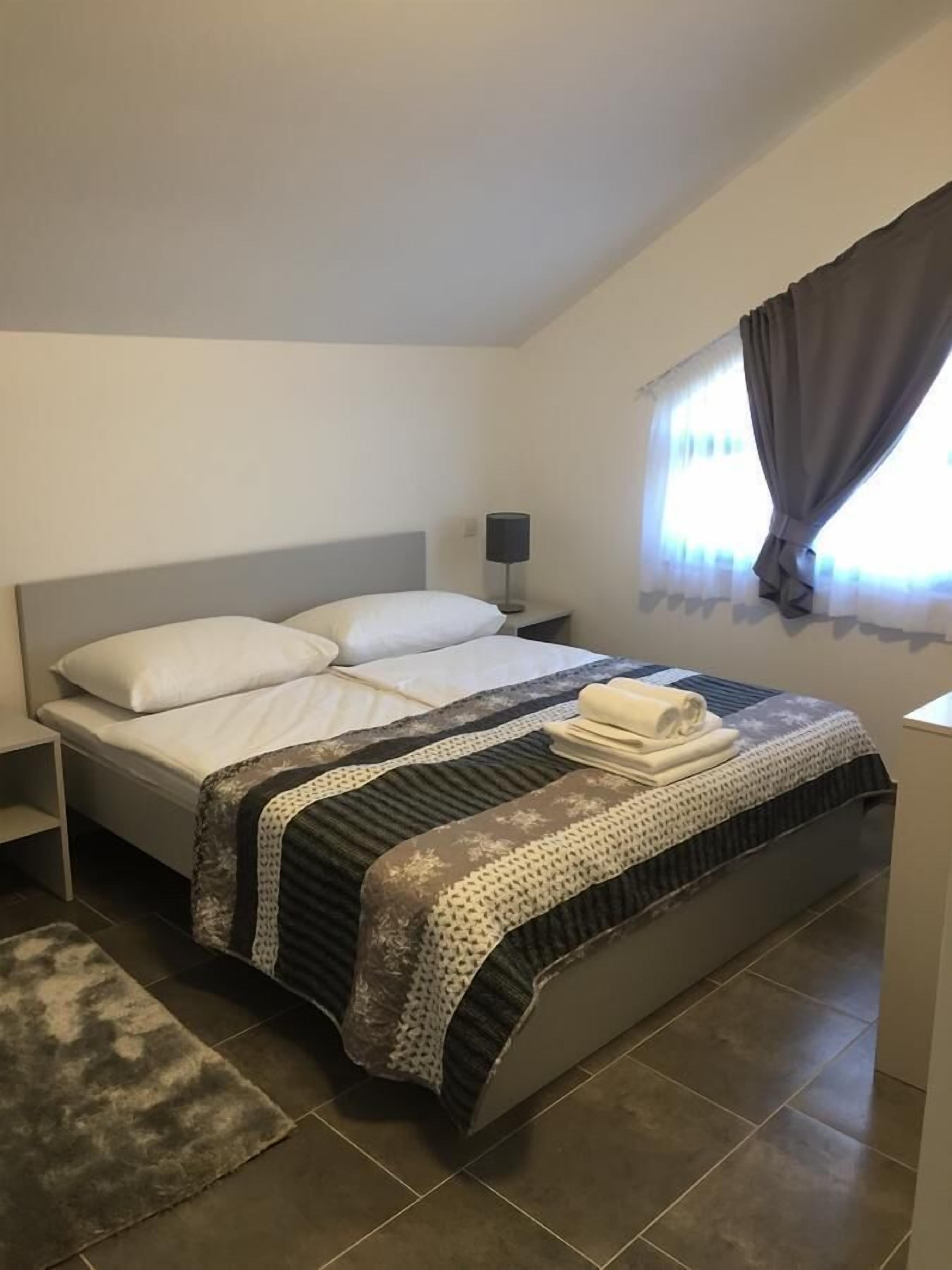 A neatly made bed with a patterned bedspread, a bedside lamp, and a window with curtains.