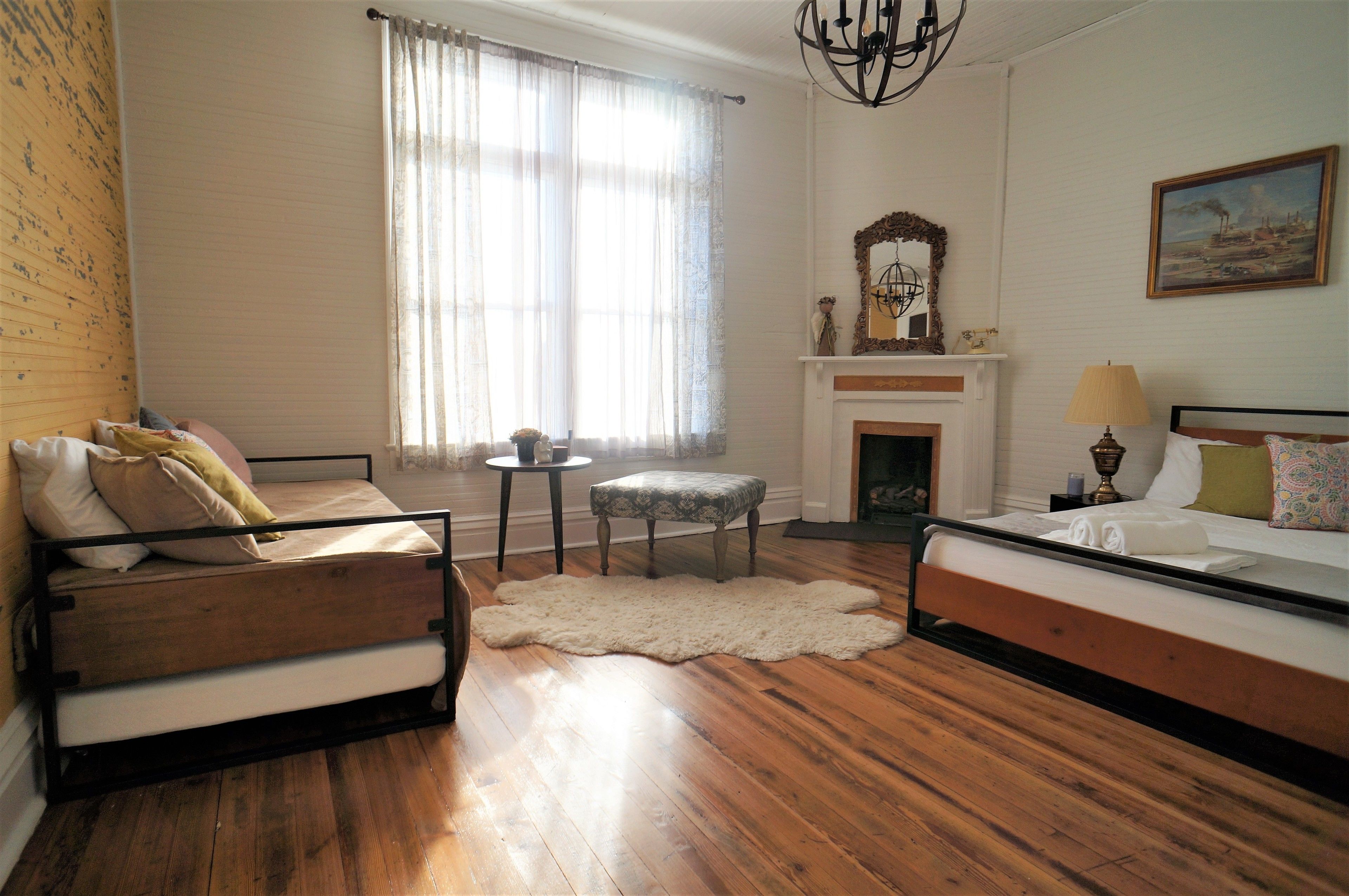 Una habitación con una cama, un sofá, una mesita, una silla, una chimenea y un candelabro.