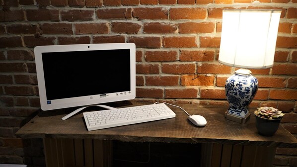 Una computadora de escritorio con monitor, teclado y ratón sobre una mesa de madera frente a una pared de ladrillo.