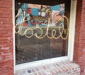 Een raam met een muurschildering van een cartoon personage en de tekst 'Hostel' in verlichte letters.
