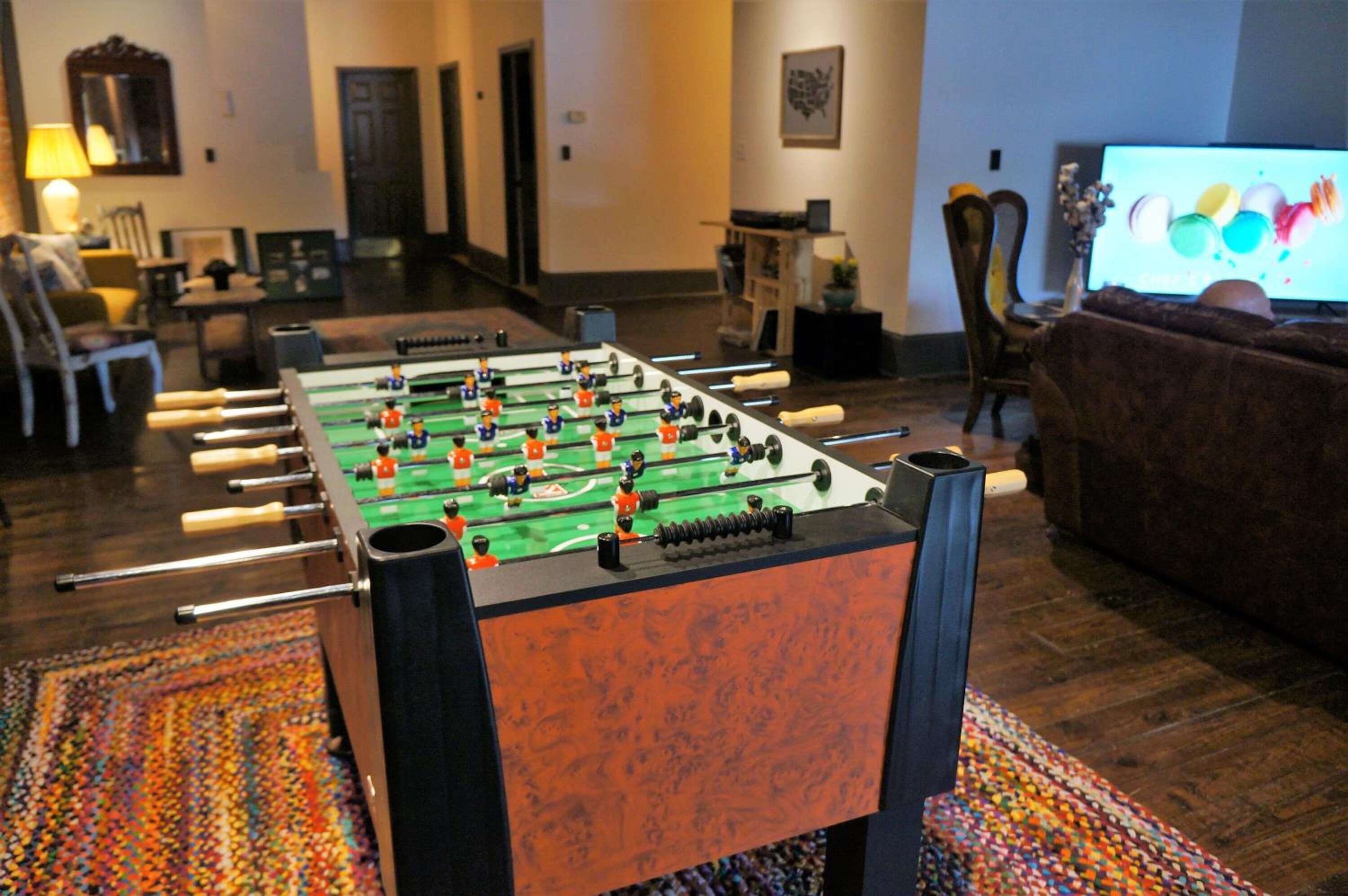 Une table de baby-foot dans une pièce équipée d’un téléviseur, d’un canapé et d’un tapis à motifs.