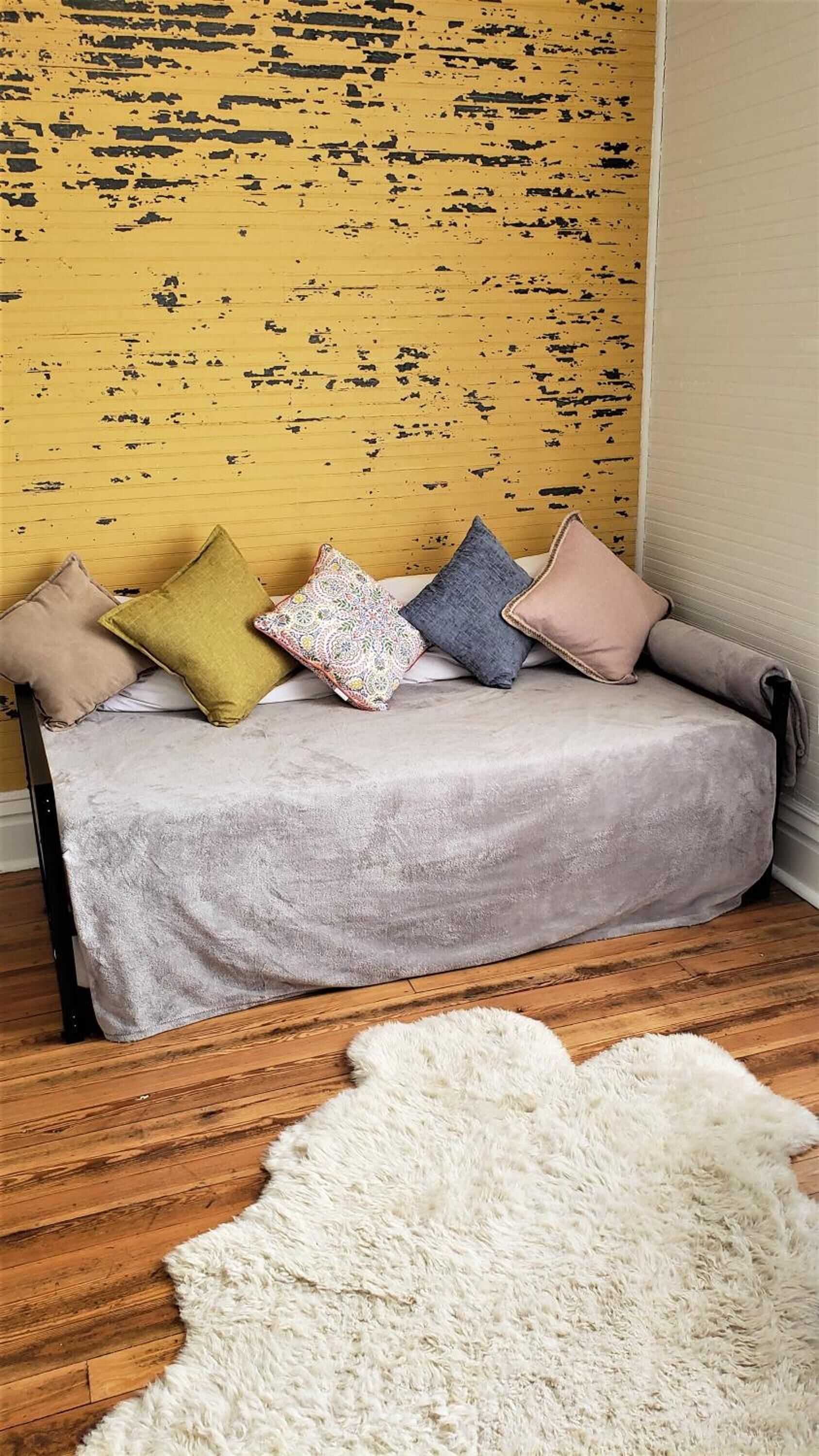 A sofa with multiple cushions against a yellow wall with black paint splatters.