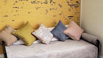 A sofa with multiple cushions against a yellow wall with black paint splatters.