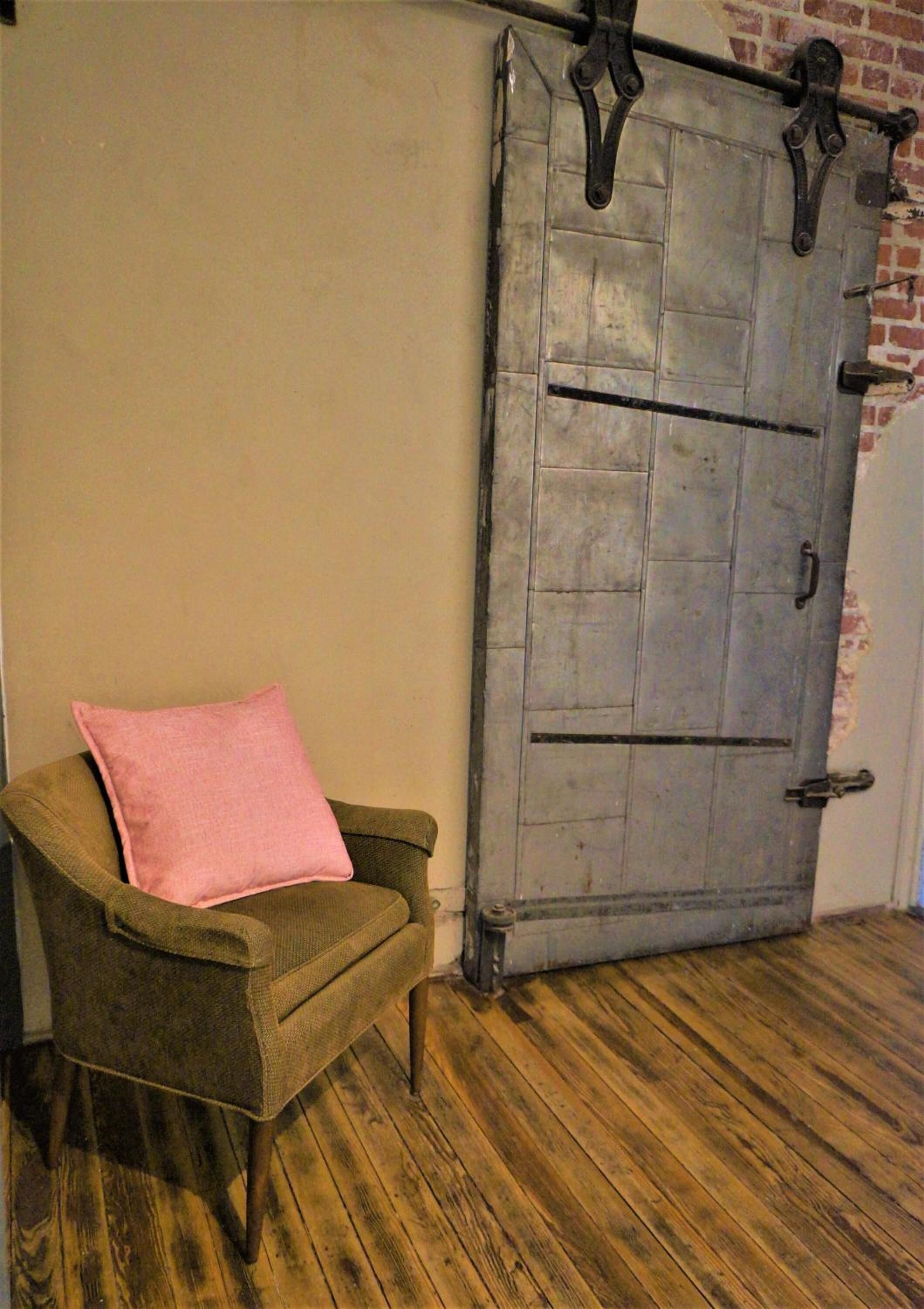 Une chaise avec un coussin rose, un plancher en bois et une grande porte en métal dotée d’une poignée.