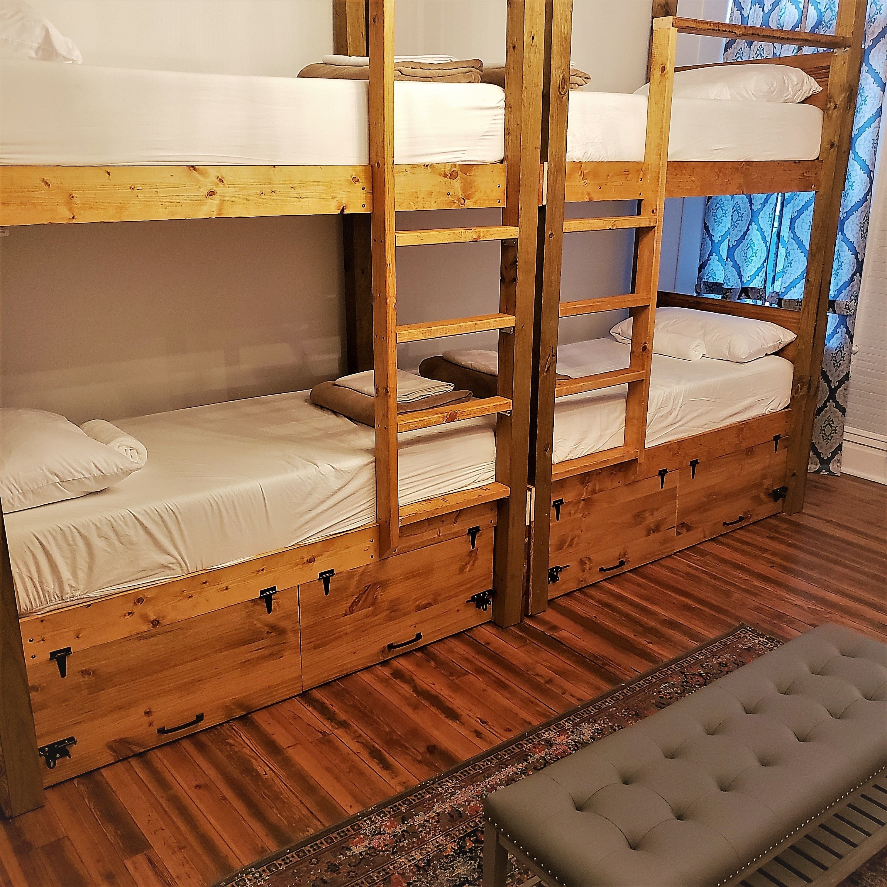 A bunk bed room with wooden frames, a bench, and a patterned rug.