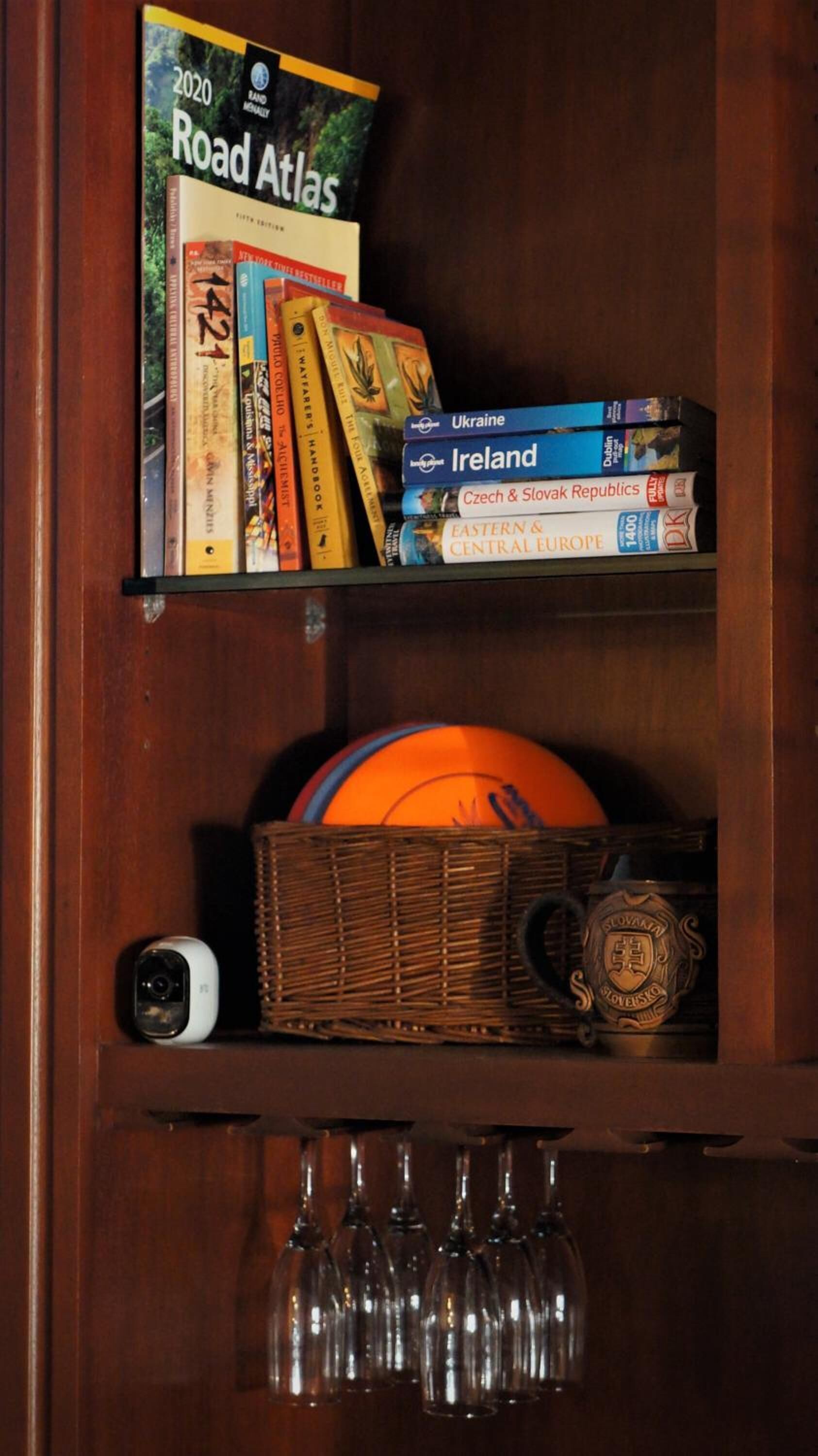 Una repisa de madera con un atlas de carreteras, guías de viaje, una cámara y copas de vino.