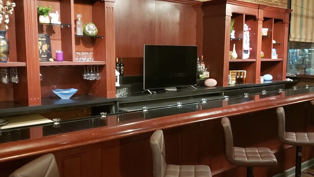 Un área de bar con taburetes de madera y estantes con botellas y vasos.