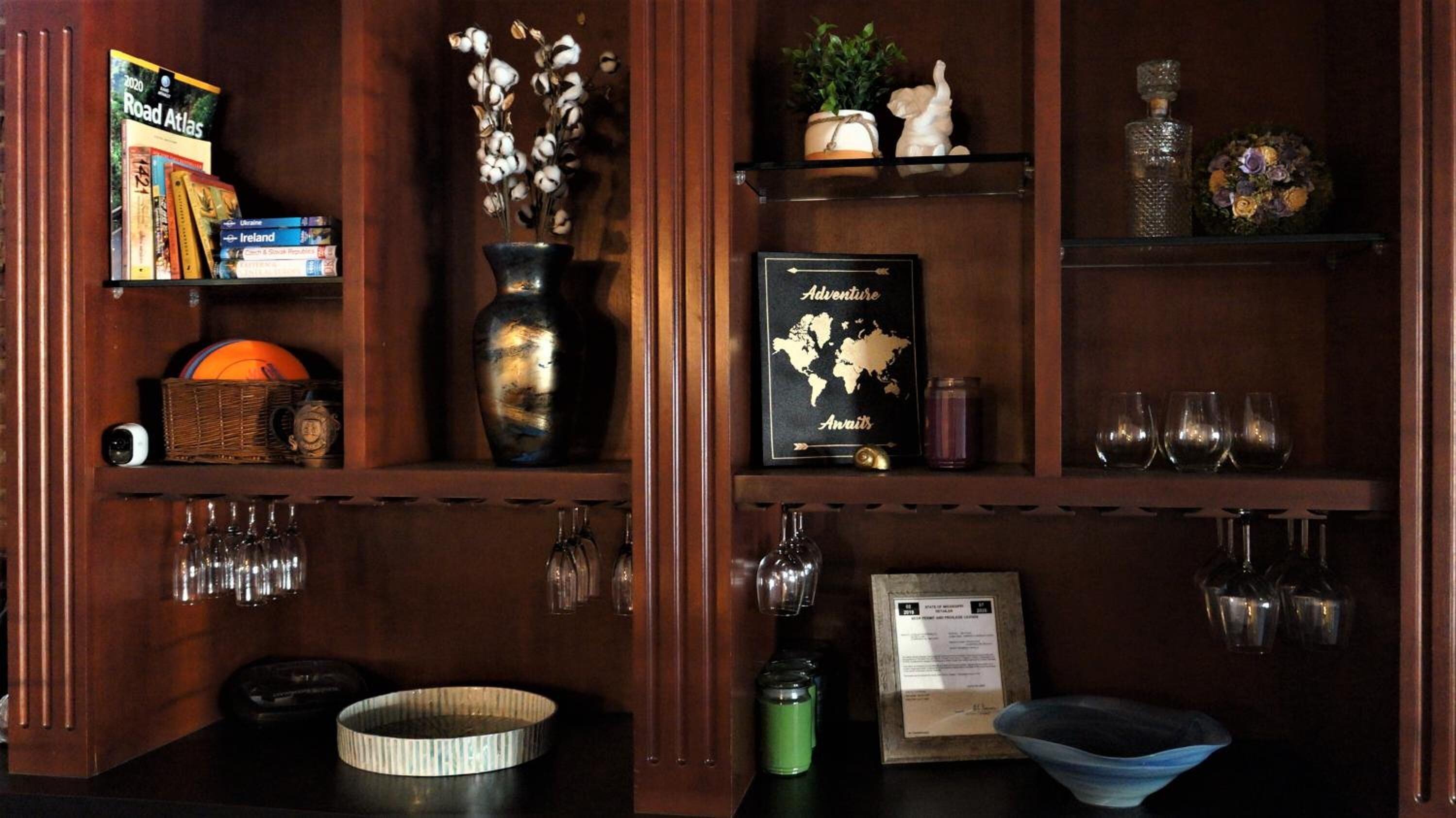 Ein Holzregal mit Büchern, einer Vase mit Trockenblumen, einer gerahmten Karte und verschiedenen Glaswaren.