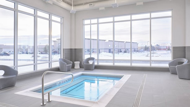 A large indoor swimming pool with clear windows, grey chairs, and a view of a snowy parking lot. - TownePlace Suites by Marriott Medicine Hat (Medicine Hat)