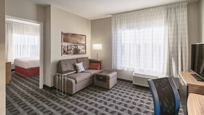 A hotel room with a sofa, a small table, a chair, a bed, a TV, and a window with curtains. - TownePlace Suites by Marriott Medicine Hat (Medicine Hat)