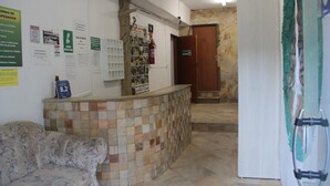 Un área de recepción con mostrador de baldosas, un sofá y varios carteles informativos en las paredes.