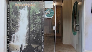 Un área de recepción con un cartel de una cascada, un letrero que indica la recepción y una puerta de cristal que da acceso al edificio.
