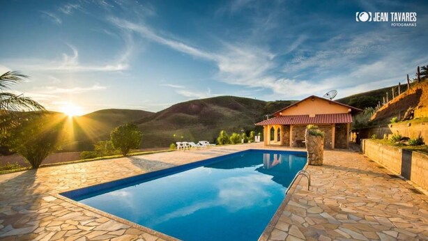 Una piscina con piastrelle in pietra, un edificio con tetto rosso e un paesaggio montuoso sullo sfondo.