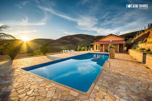 Una piscina con baldosas de piedra, un edificio con techo rojo y un paisaje montañoso al fondo.