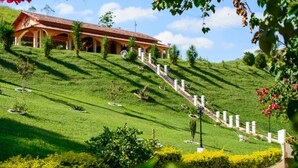 Una casa su una collina con tetto in tegole rosse, recinzione bianca e prato curato.