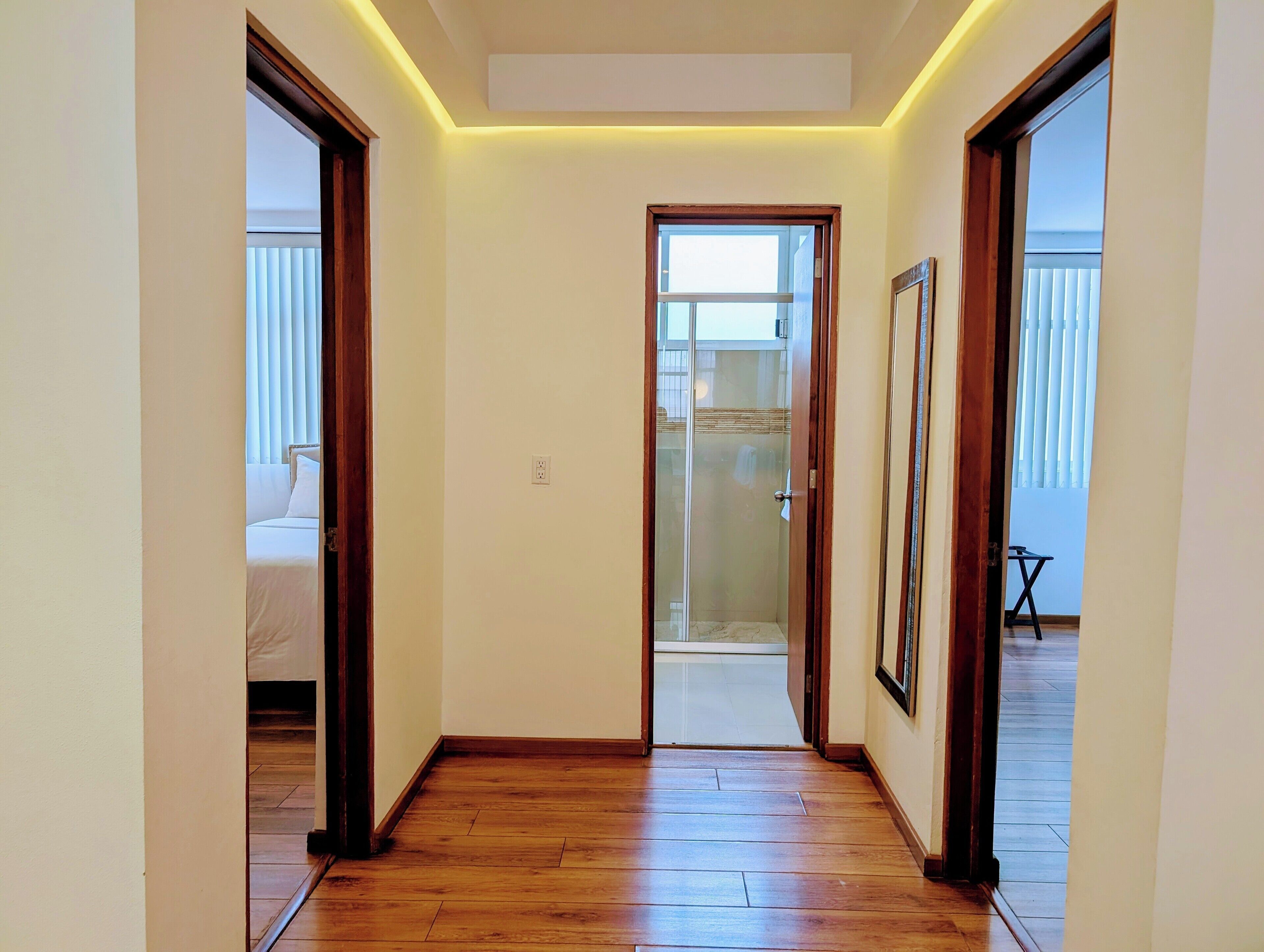 A hallway with wooden flooring, a glass door leading to a balcony, and a bed visible through an open door.