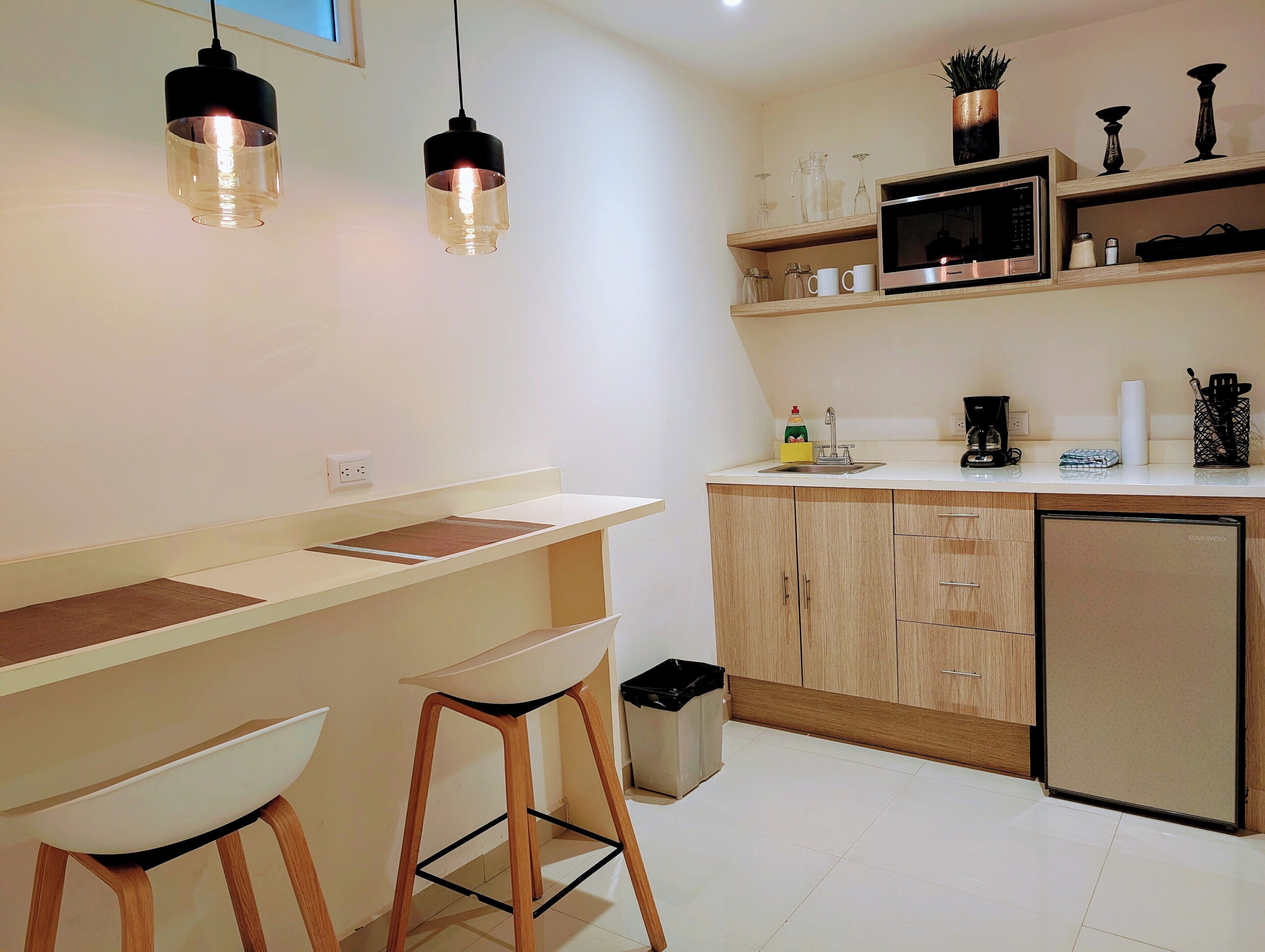 A modern kitchen with a white countertop, wooden cabinets, a microwave, and two bar stools.