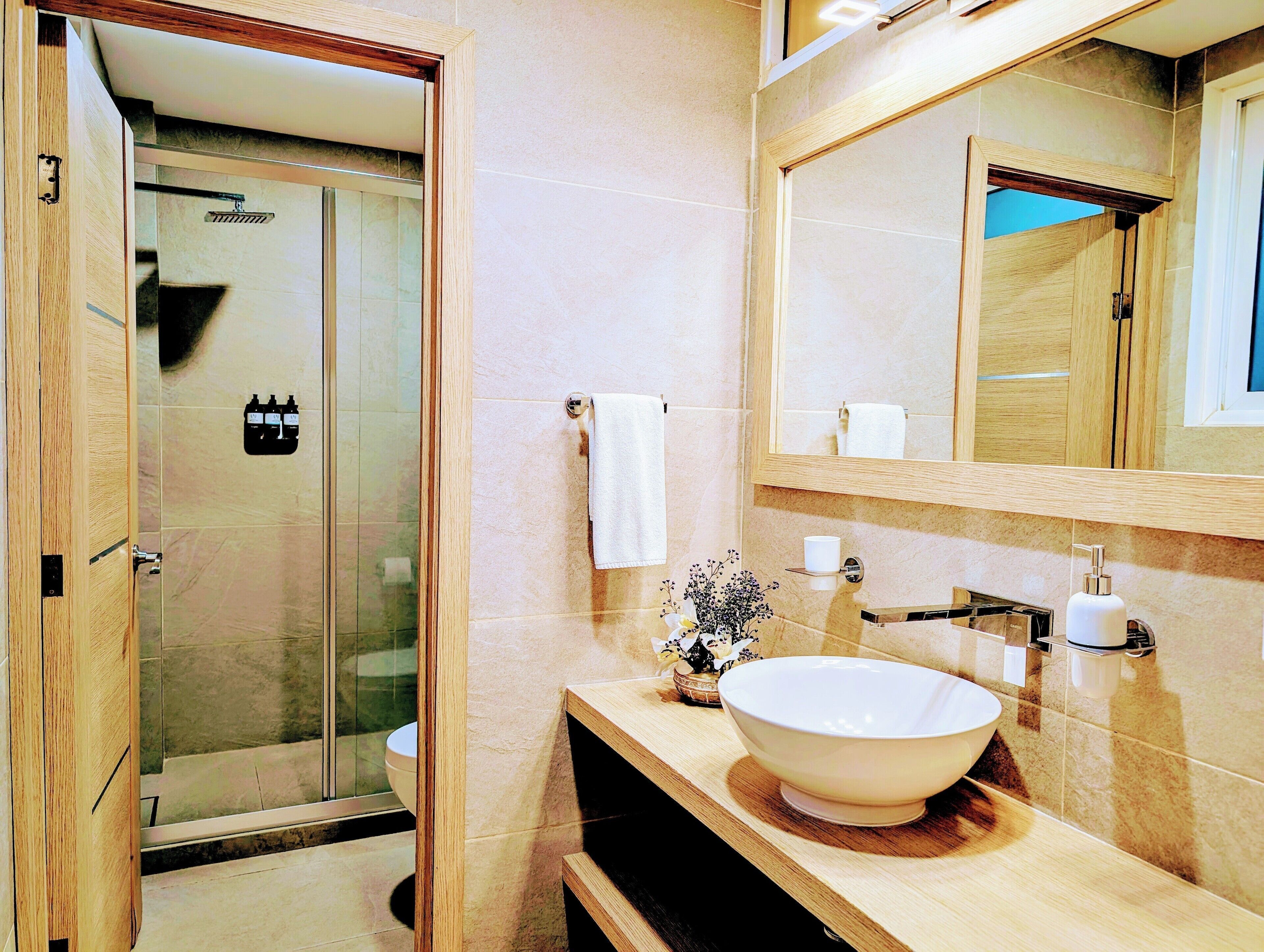 Un baño moderno con ducha de vidrio, un espejo grande y un tocador de madera con lavabo.