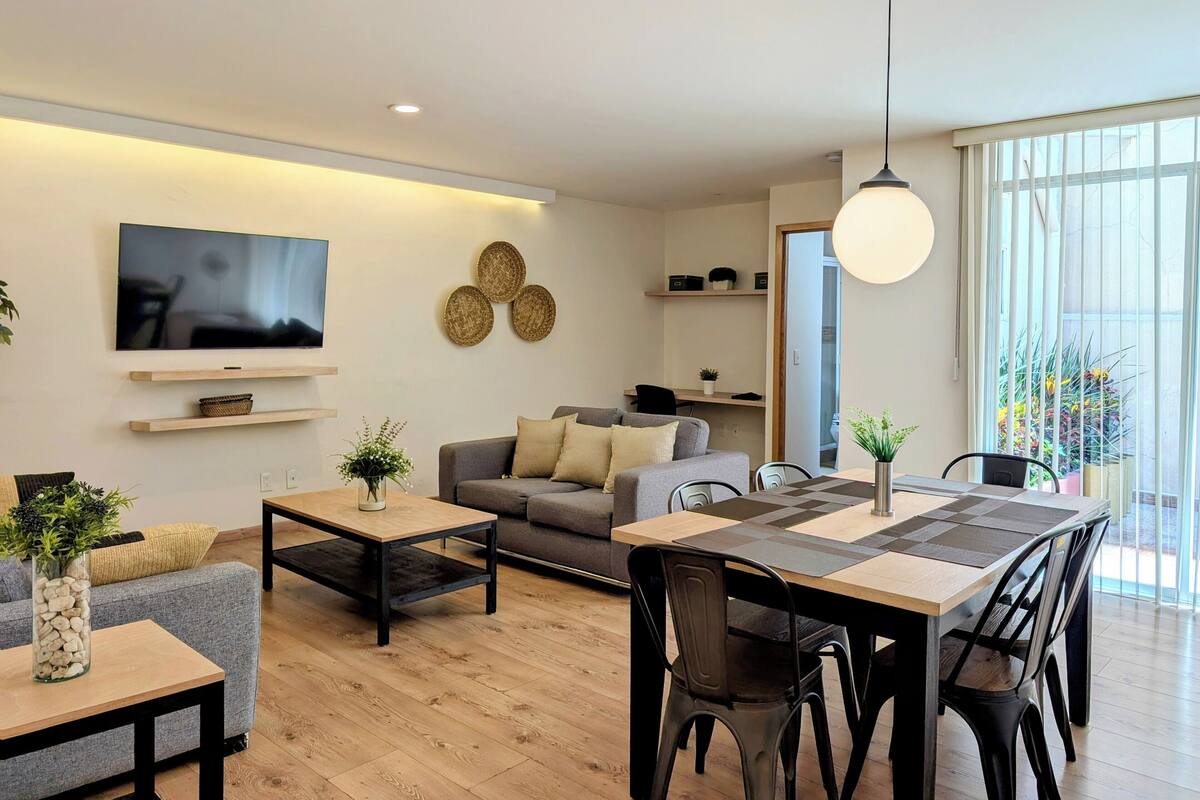 Una sala de estar moderna con sofá, mesa de centro, televisor y comedor.