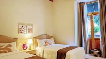 A hotel room with two beds, a wooden headboard, a nightstand with a lamp, artwork on the wall, and a window with curtains.