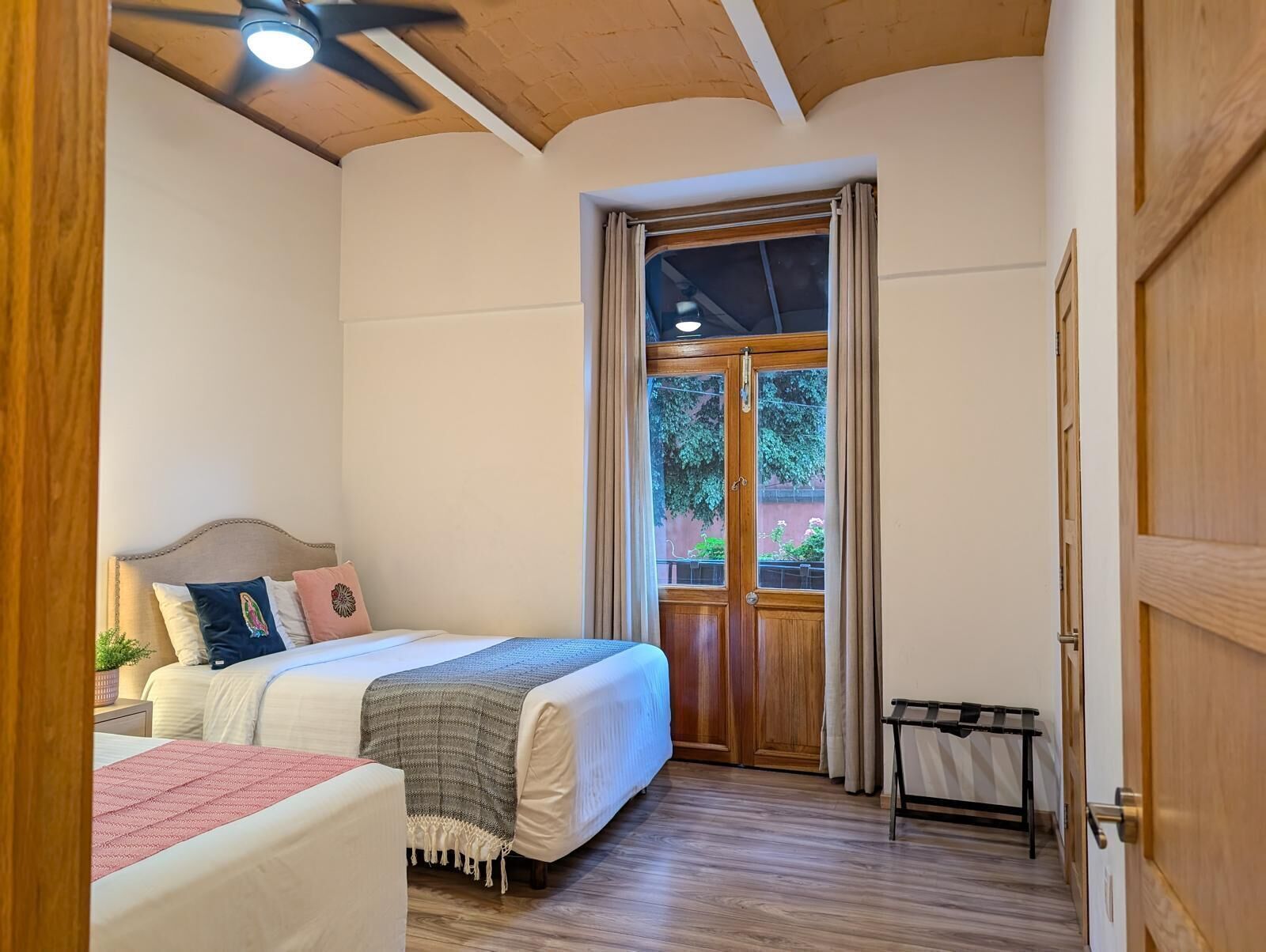 Un dormitorio con una cama, una mesita de noche, un ventilador de techo, una ventana con cortinas y una puerta.