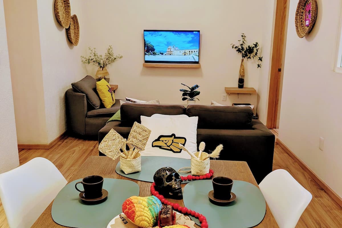 Una sala de estar moderna con un televisor de pantalla plana, un sofá y una mesa de comedor decorada con un centro de mesa colorido.