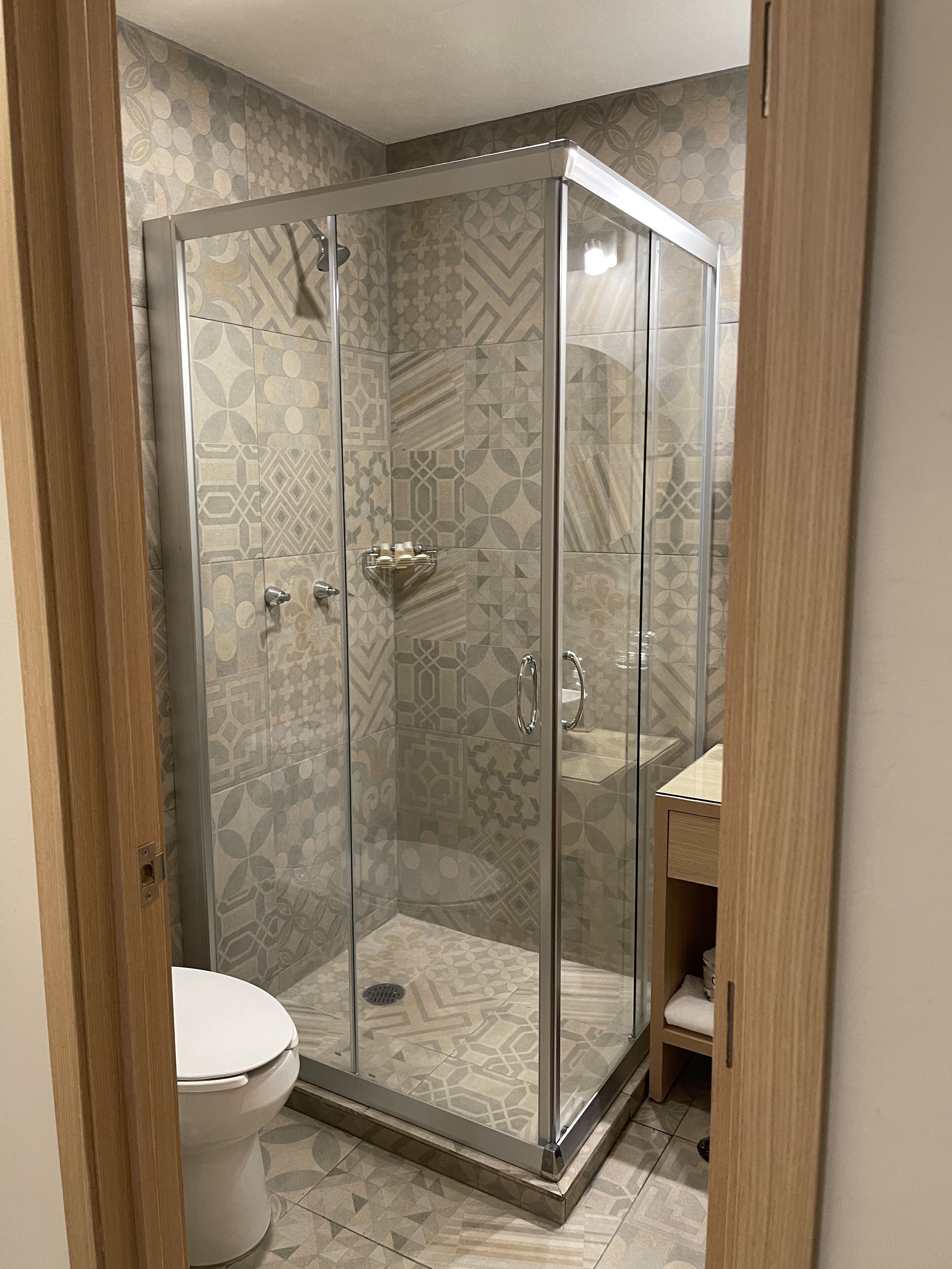 A shower enclosure with a glass door, a toilet, and a sink with a wooden cabinet.