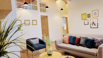 A modern living room with a sofa, armchairs, and a coffee table. There are framed pictures on the wall and a plant on the floor.