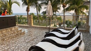 A sun loungers area with a view of the ocean, palm trees, and a stone staircase. - Hotel Villa Murano (Tonalá)