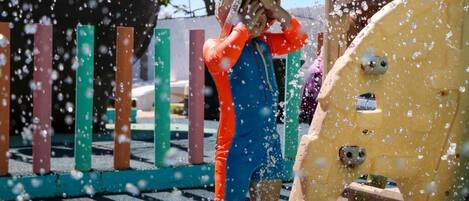 A person in a blue and orange outfit near a yellow structure with water spraying.