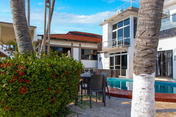 A pool area with a white building, outdoor seating, and palm trees.