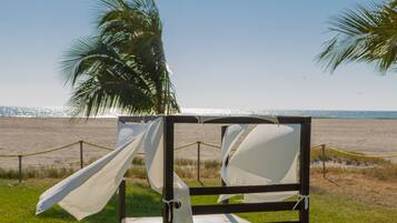 Una cama frente a la playa, con vista al océano, una palmera y una barrera de cuerda.