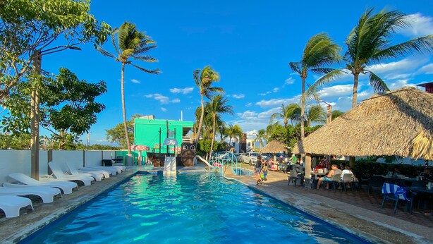 A swimming pool with lounge chairs, palm trees, and a thatched-roof structure. - Hotel Villa Murano (Tonalá)