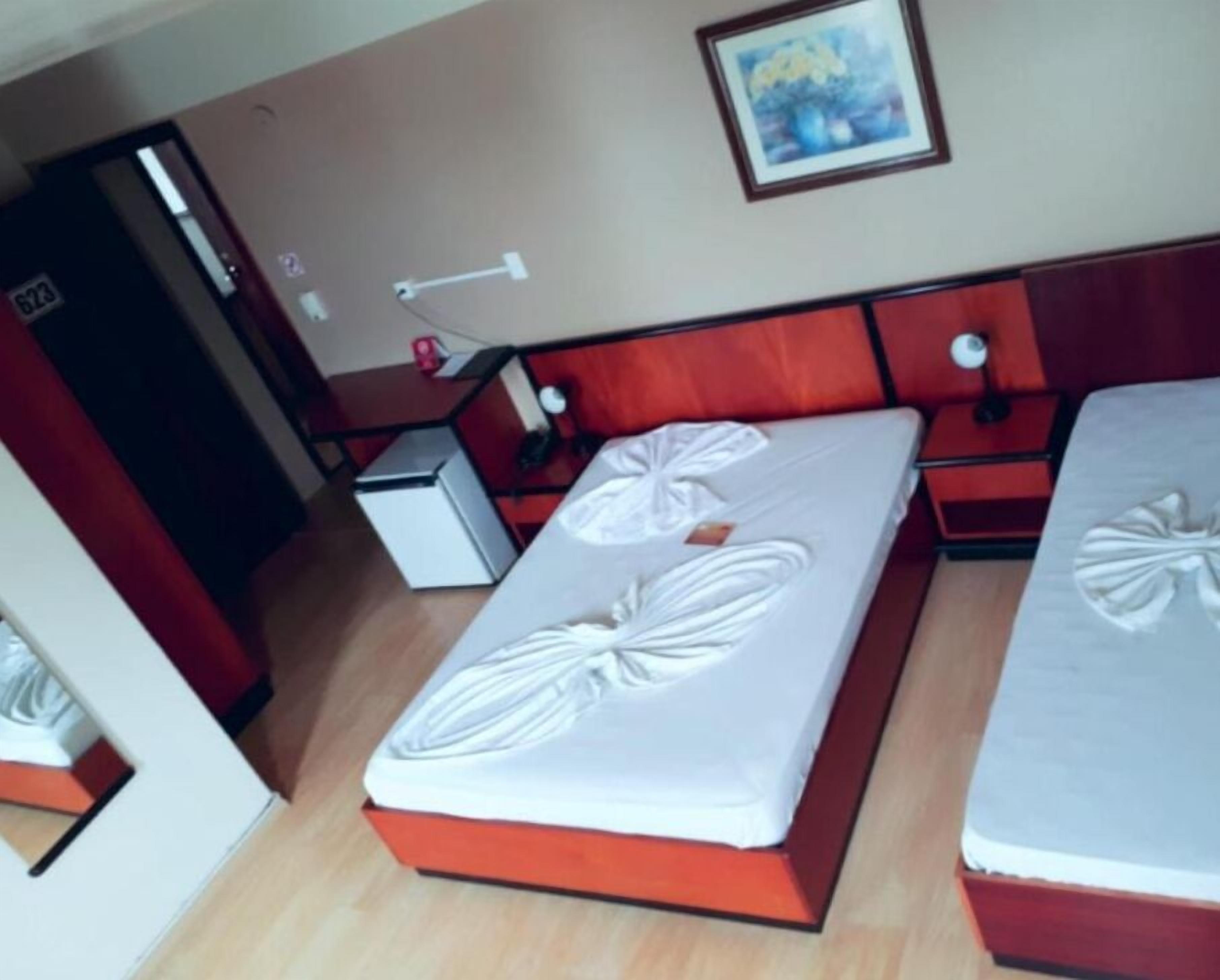 Quarto de hotel com duas camas, uma secretária pequena e uma porta.