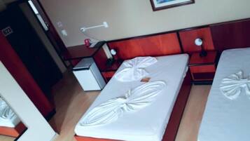 Quarto de hotel com duas camas, uma secretária pequena e uma porta.