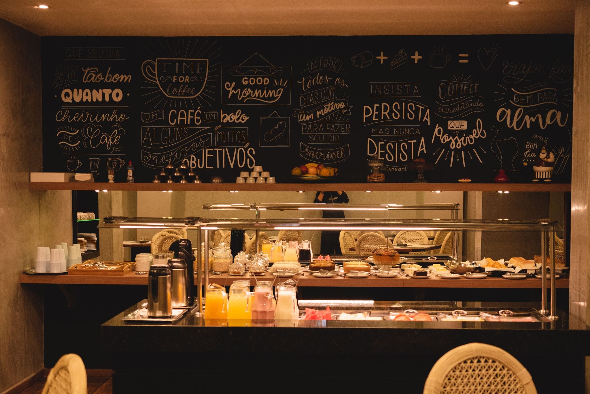Un espace buffet pour le petit-déjeuner avec un mur noir où sont écrites différentes phrases inspirantes, ainsi qu’une machine à café.
