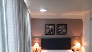 Une chambre d’hôtel avec un lit, deux lampes de chevet, une tête de lit et deux tableaux encadrés accrochés au mur.