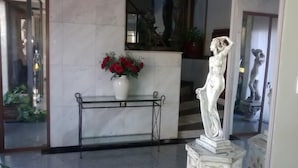 Un hall d’accueil en marbre agrémenté d’une statue, d’un vase rempli de fleurs rouges et d’une console en métal.