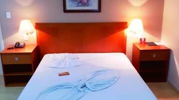 A hotel room with a bed, two bedside tables, a framed picture on the wall, and a lamp on each table.