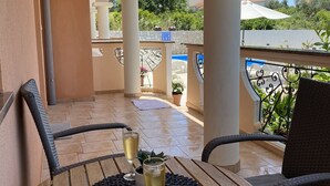 Een houten tafel met twee champagneglazen op een balkon met witte zuilen en een uitzicht op groen en huizen op de achtergrond.
