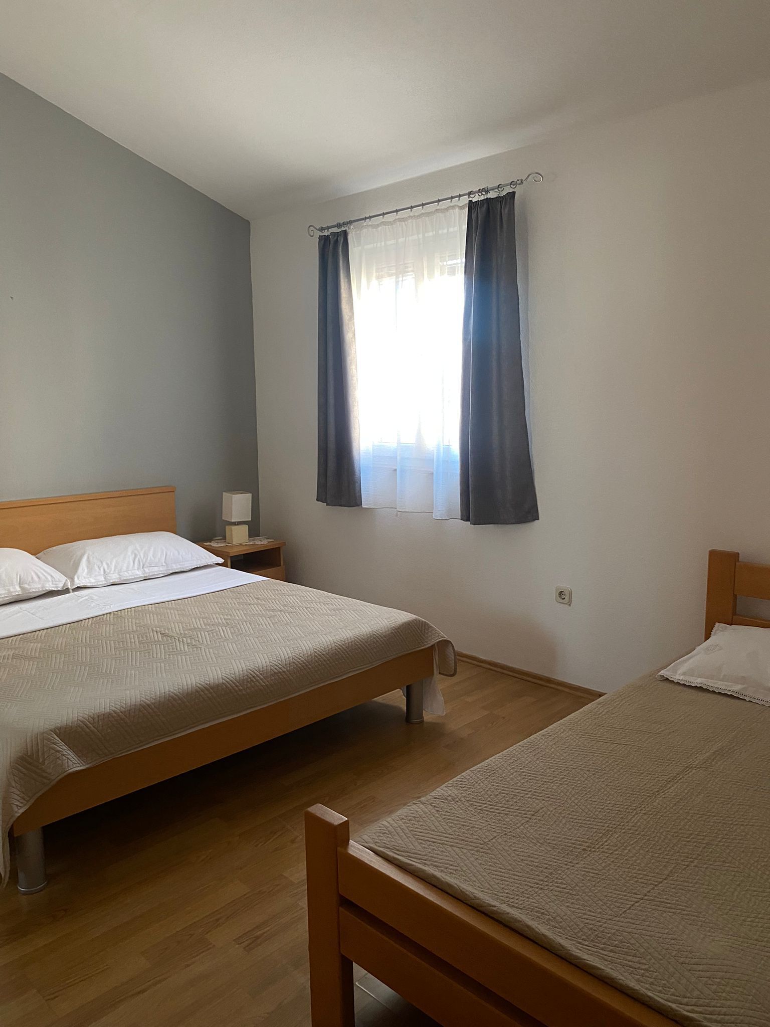 A room with two beds, a nightstand, a lamp, and a window with curtains.