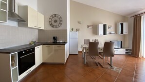 Een moderne keuken met een fornuis, oven en witte kasten. Er is een eethoek met een tafel en stoelen.