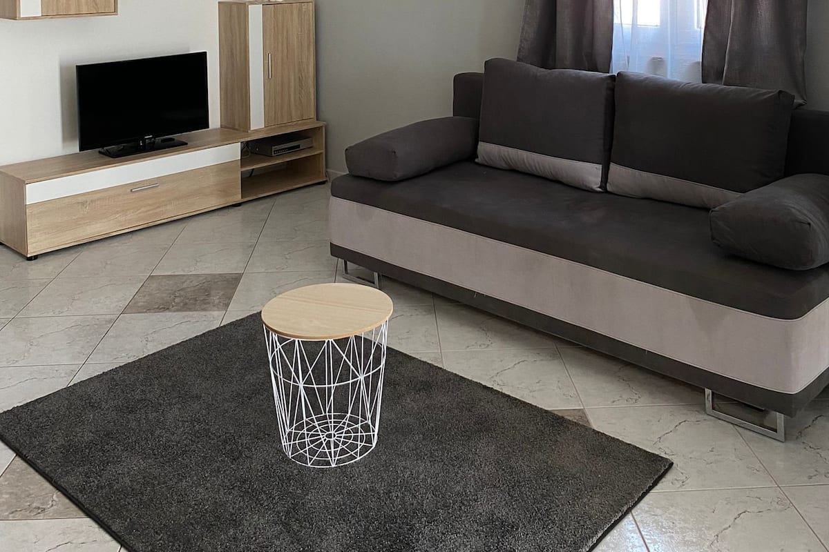 Een moderne woonkamer met een grijze bank, een flatscreen televisie, houten kasten en een plafondlamp.
