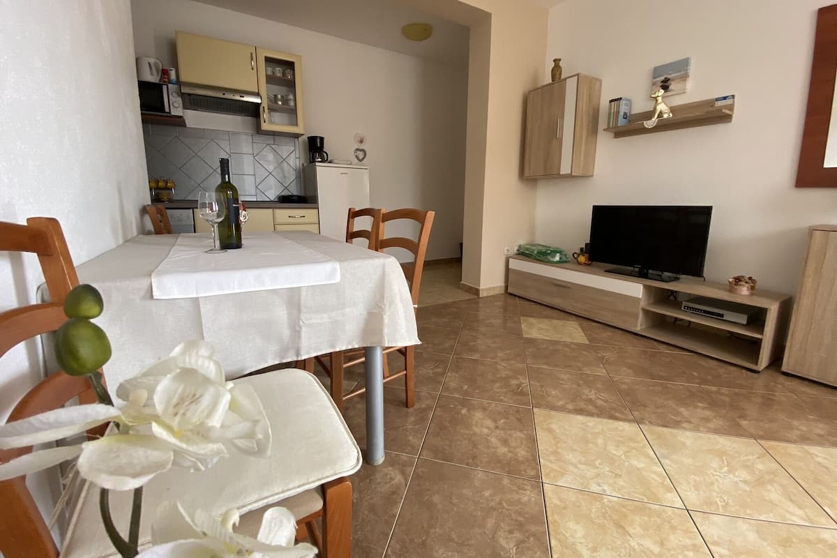 Een eetruimte met een tafel gedekt voor twee personen, een keuken op de achtergrond en een televisie op een houten standaard.
