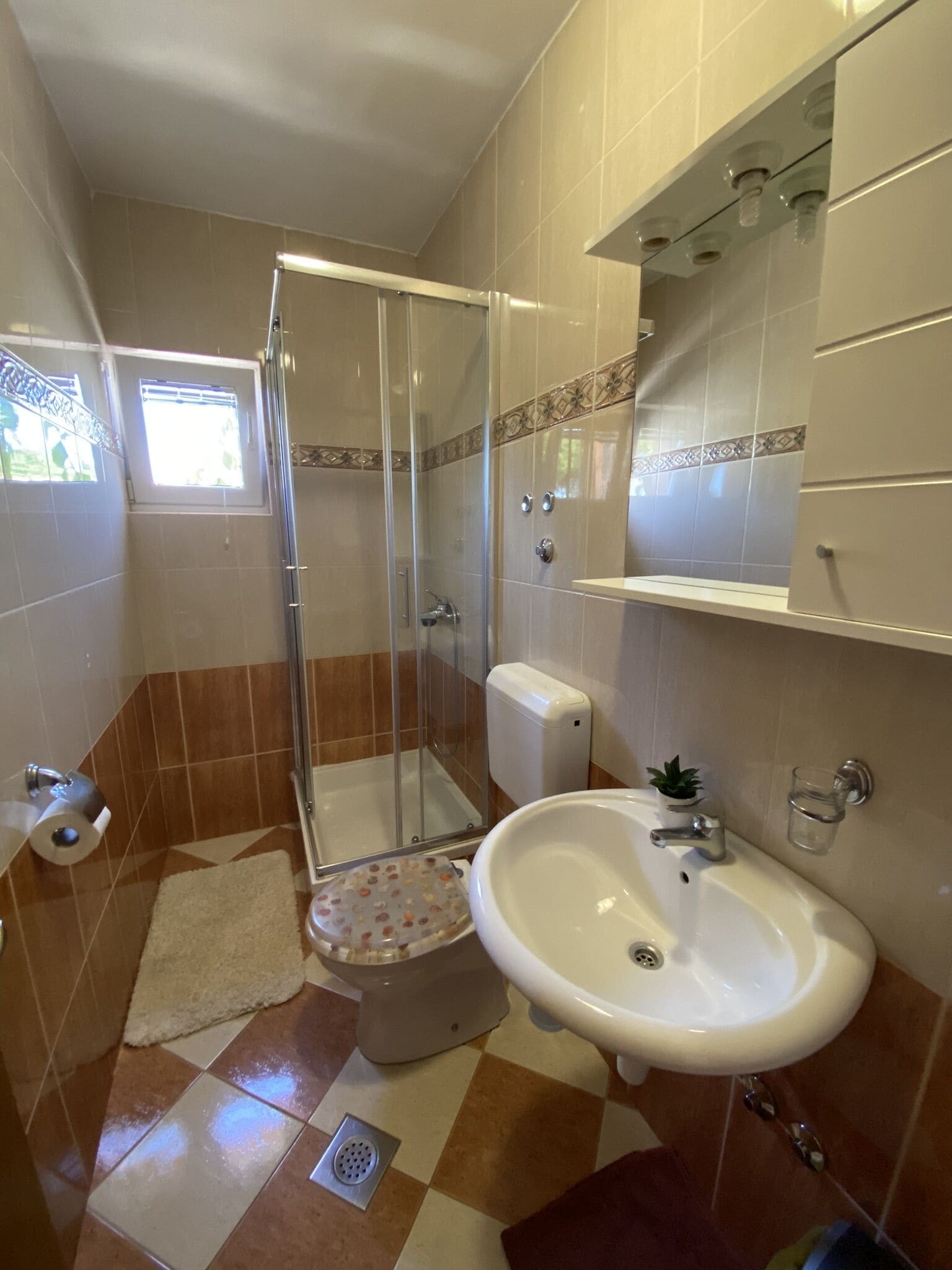 Baño con ducha, inodoro, lavamanos y una ventana pequeña.