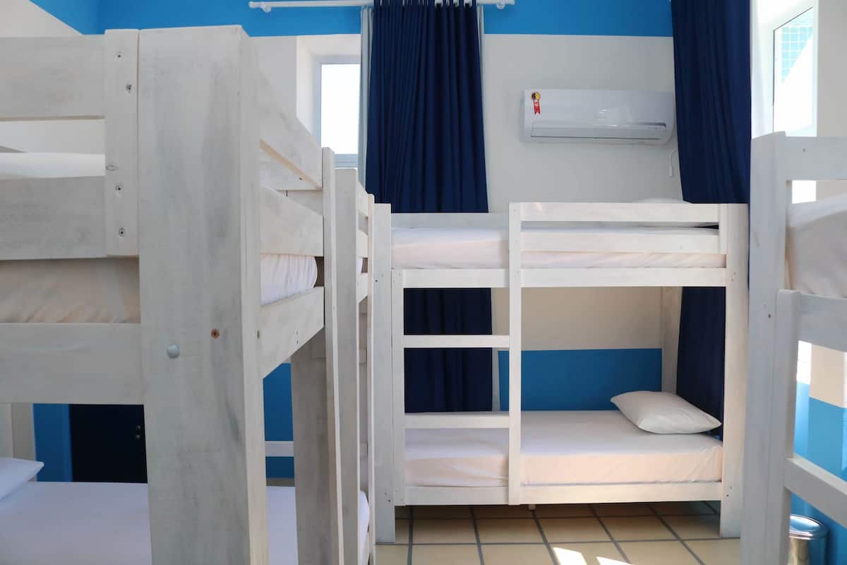 Une chambre avec un lit superposé, une fenêtre, des rideaux et un appareil de climatisation.