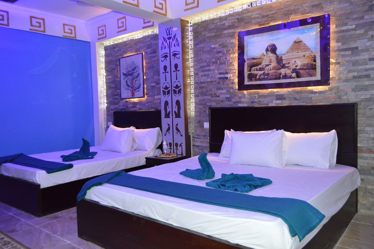 A hotel room with two beds, a stone wall, and a framed picture of pyramids.